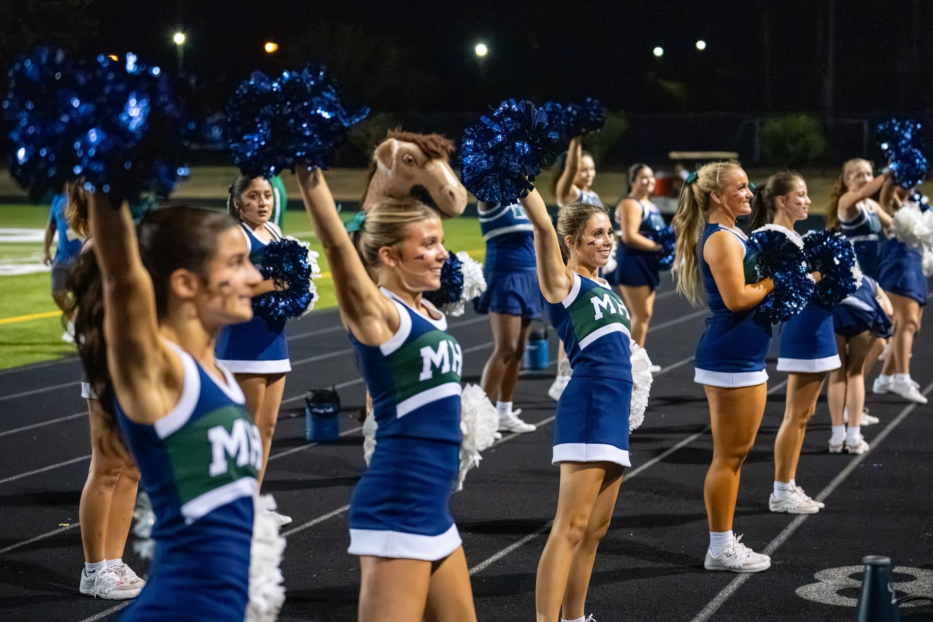 McNeil cheerleaders raising pom-poms on the sideline during a football game