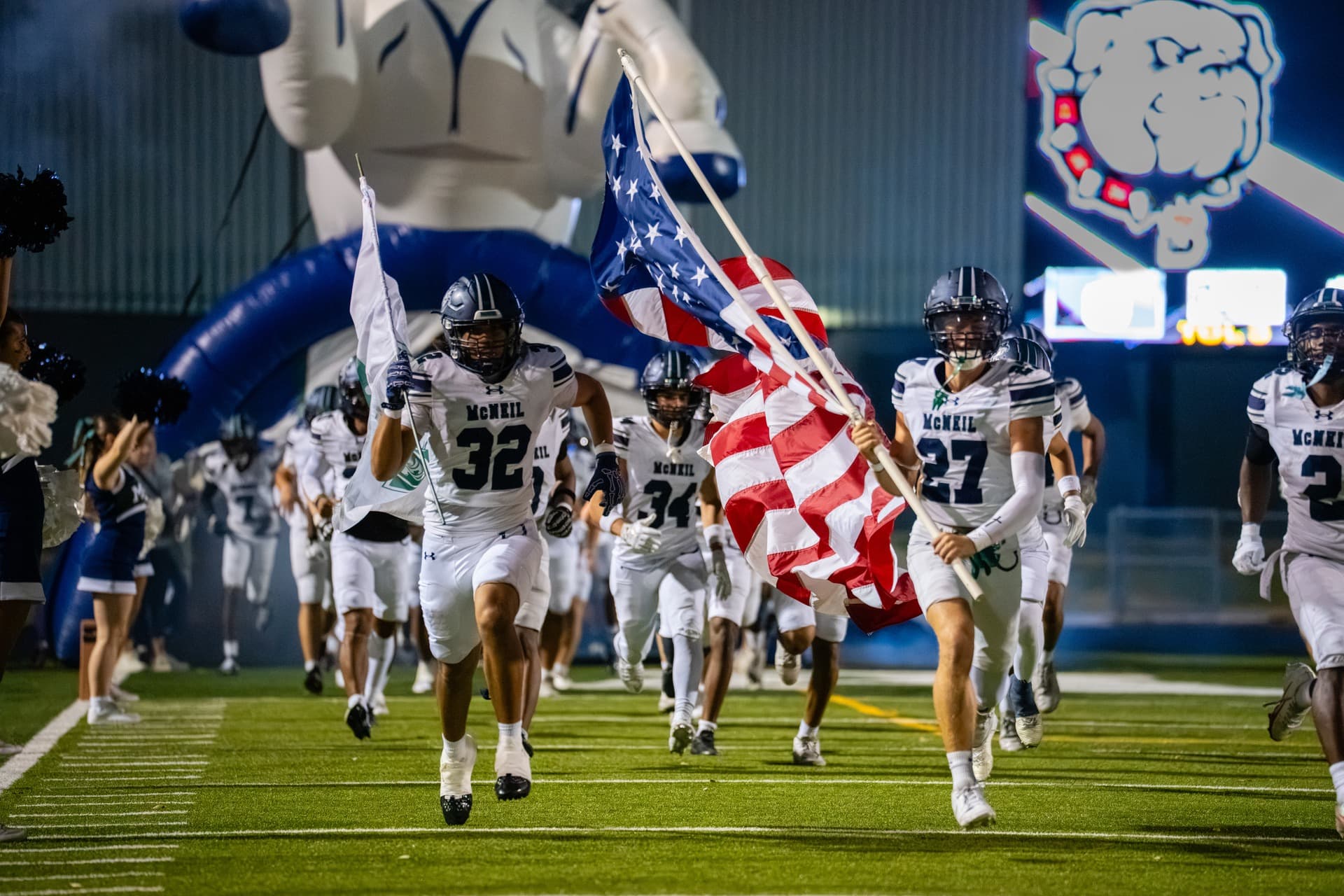 McNeil Mavericks football team running onto the field carrying the American flag